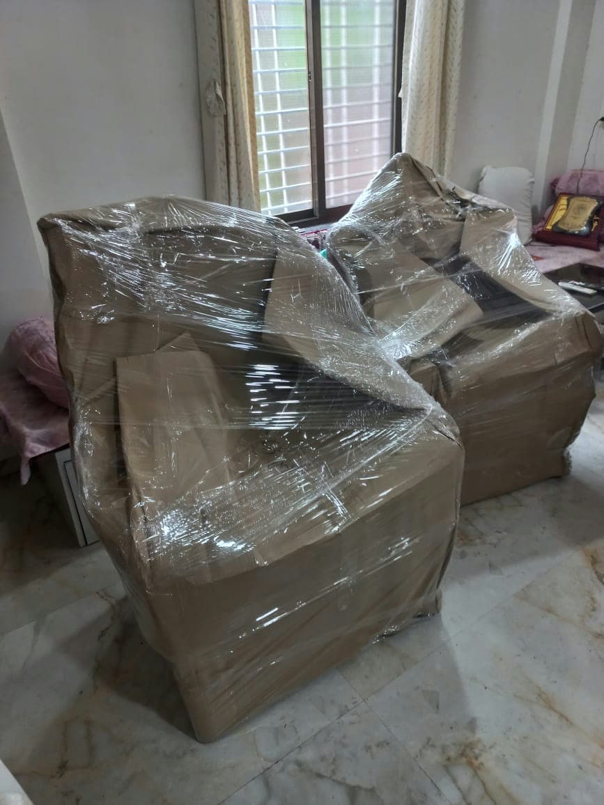 Two armchairs fully enveloped in protective cardboard and stretch film to safeguard against dirt and damage.