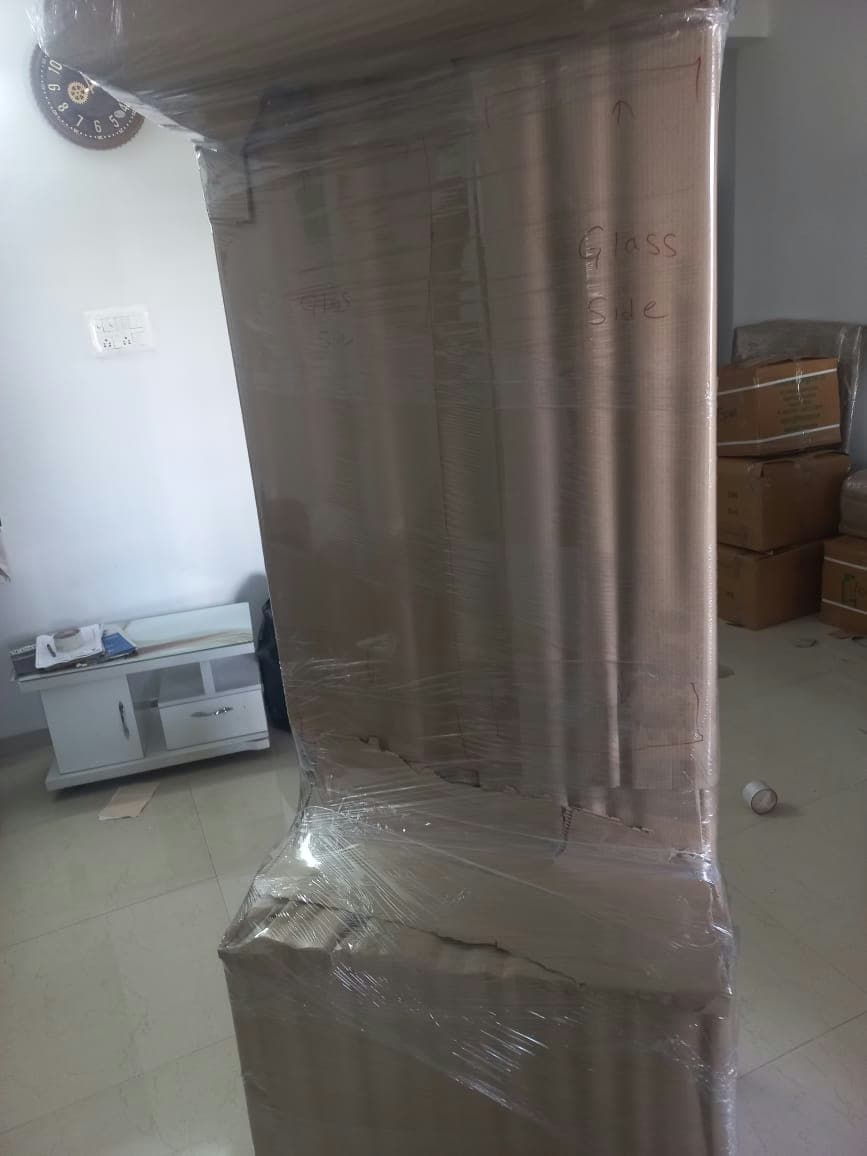 Close-up of a tall furniture piece with custom cardboard wrapping and clear 'Glass Side' handling labels.