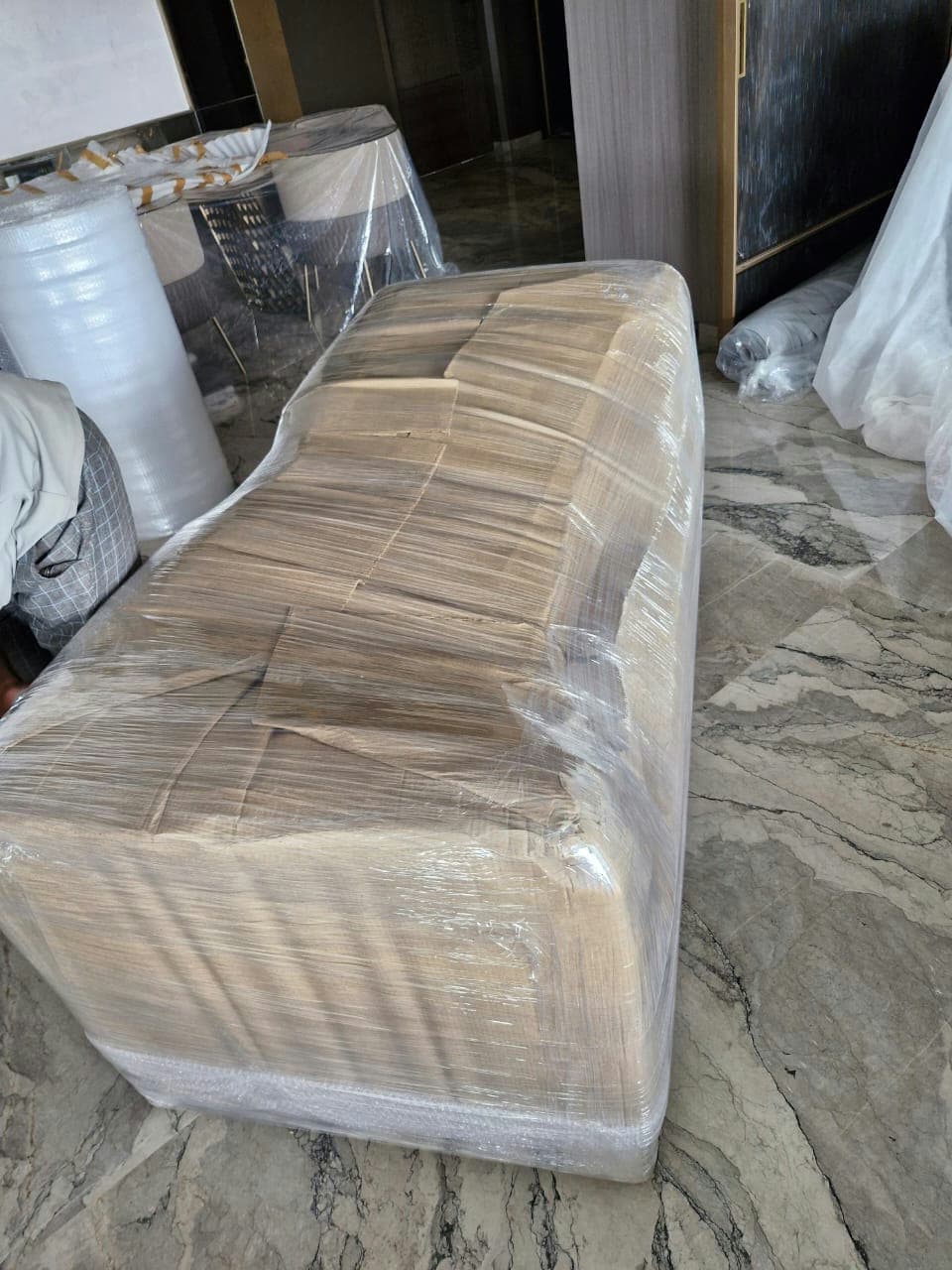 A professional mover creating a custom-fit corrugated cardboard wrap for a large sofa to ensure a perfect fit.